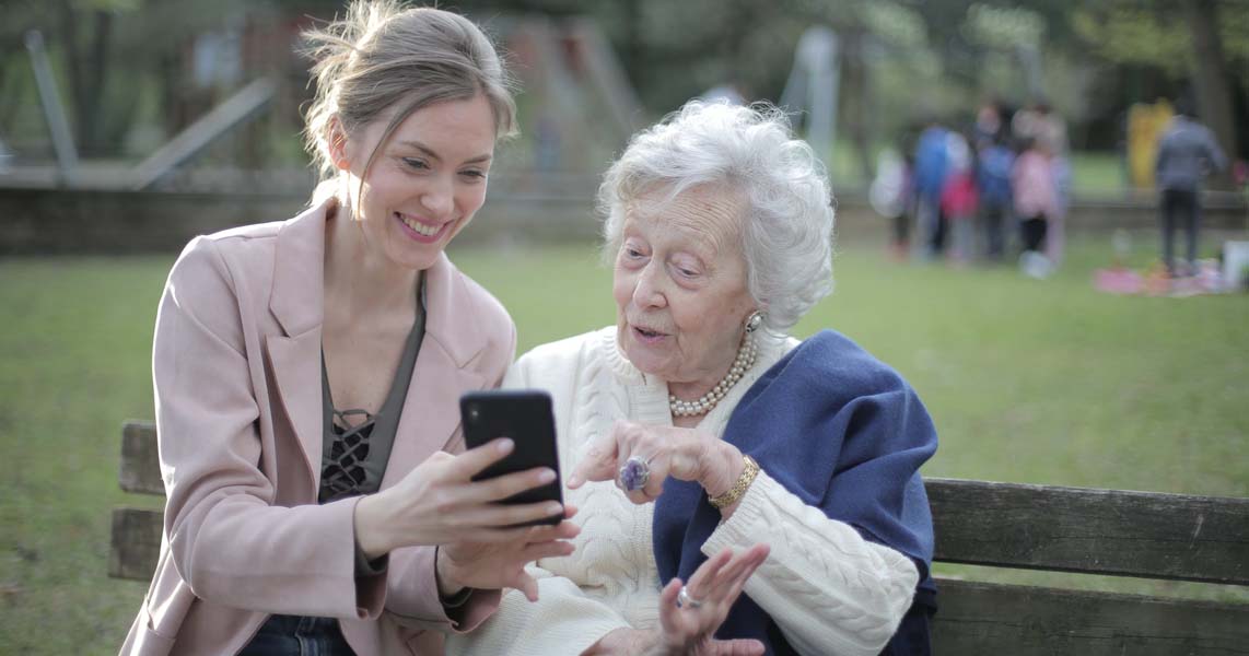 A cheerful young woman shows an older woman how to use a smartphone